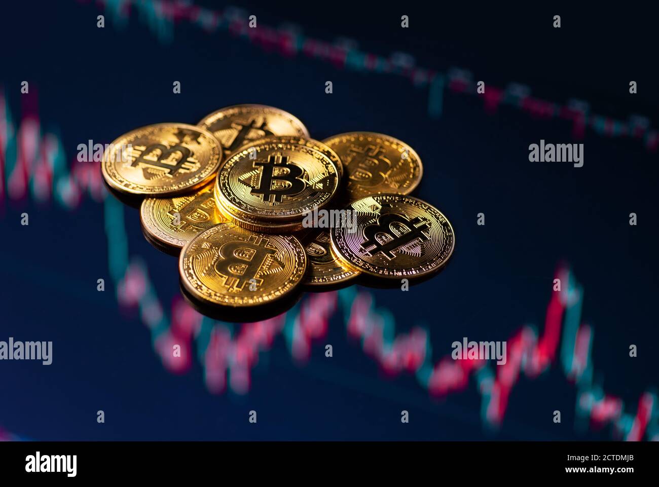 Primo piano di monete d'oro bitcoin su uno sfondo grafico di trading in discesa. Foto Stock