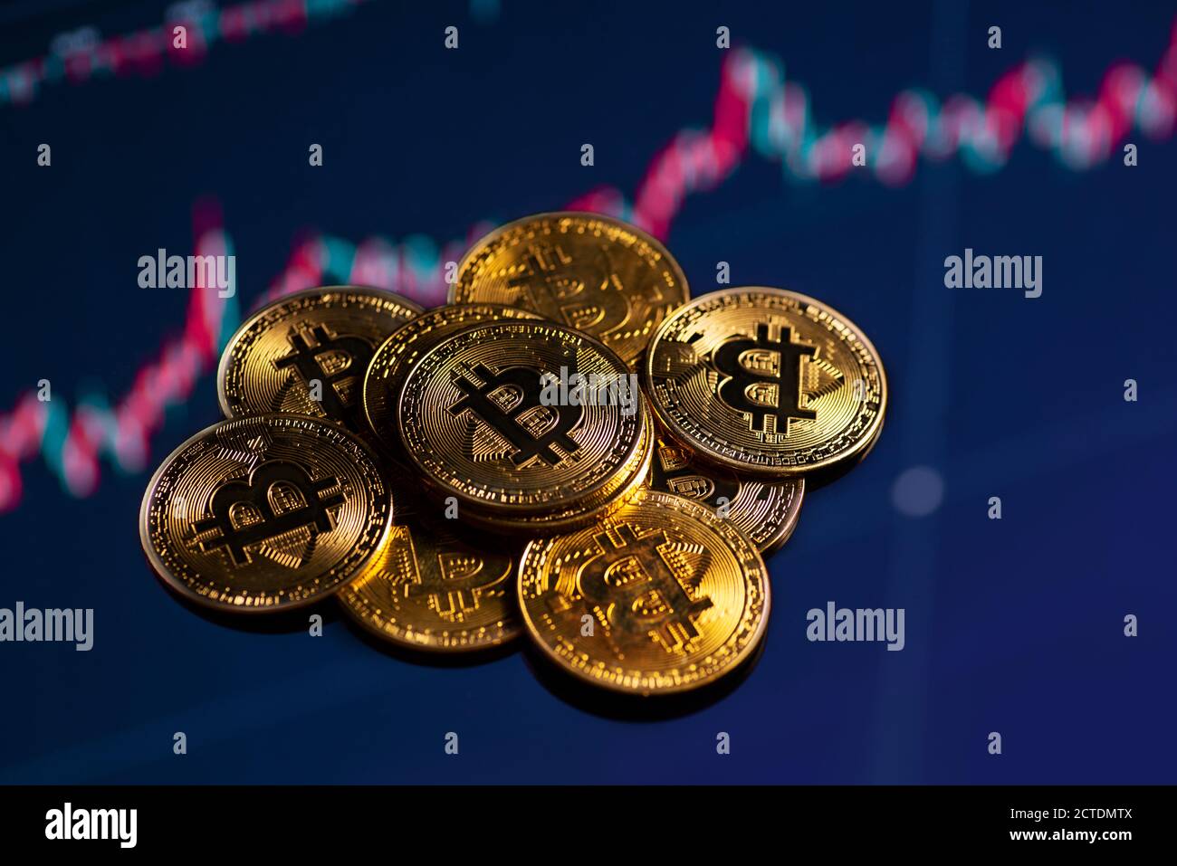 Primo piano di monete d'oro bitcoin su uno sfondo grafico di trading in corso. Foto Stock