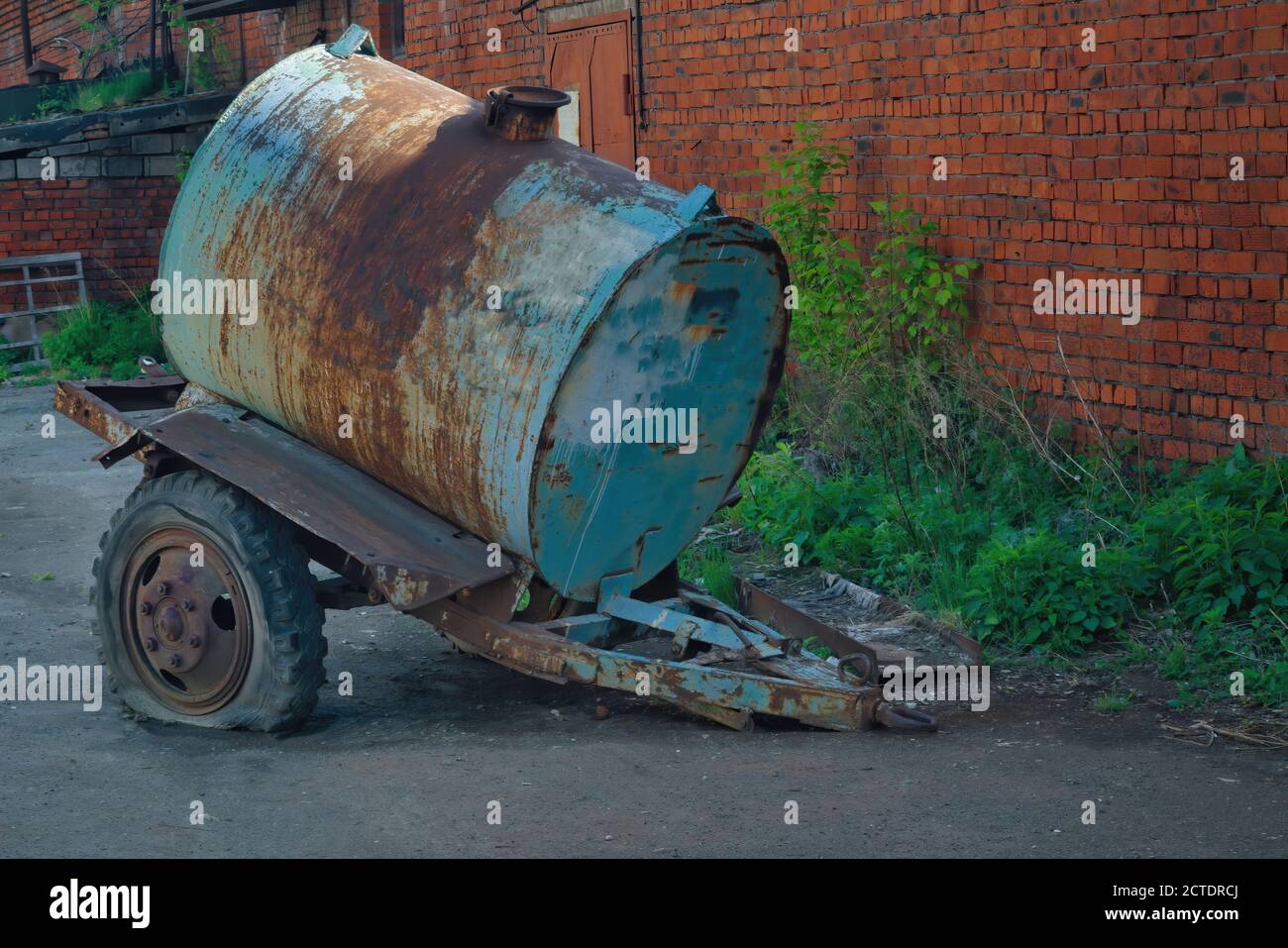 Vecchio rimorchio per autocisterna arrugginito sullo sfondo della parete di mattoni. Foto Stock