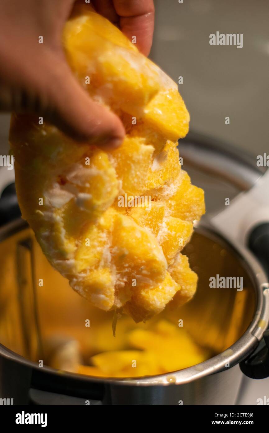 Maneggiando la frutta di mango ghiacciata per fare il gelato con l'uso di un robot da cucina o di un robot da cucina. Foto Stock
