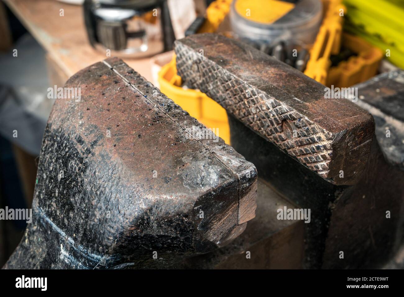 Primo piano della morsa o della morsa a ganasce. Piano di lavoro offuscato e morbido con teste a vite, nastro di misurazione e contenitori gialli. Foto Stock