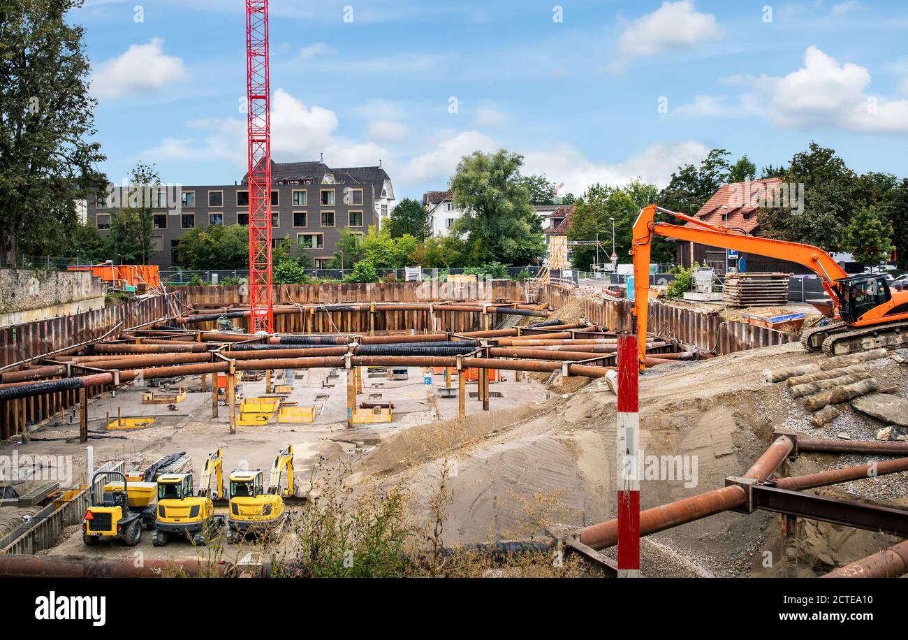 Fossa di fondazione per cantiere di edilizia residenziale o parcheggio. Tubi come distanziatori di grandi buca, gru rossa, escavatori gialli e arancioni. Foto Stock