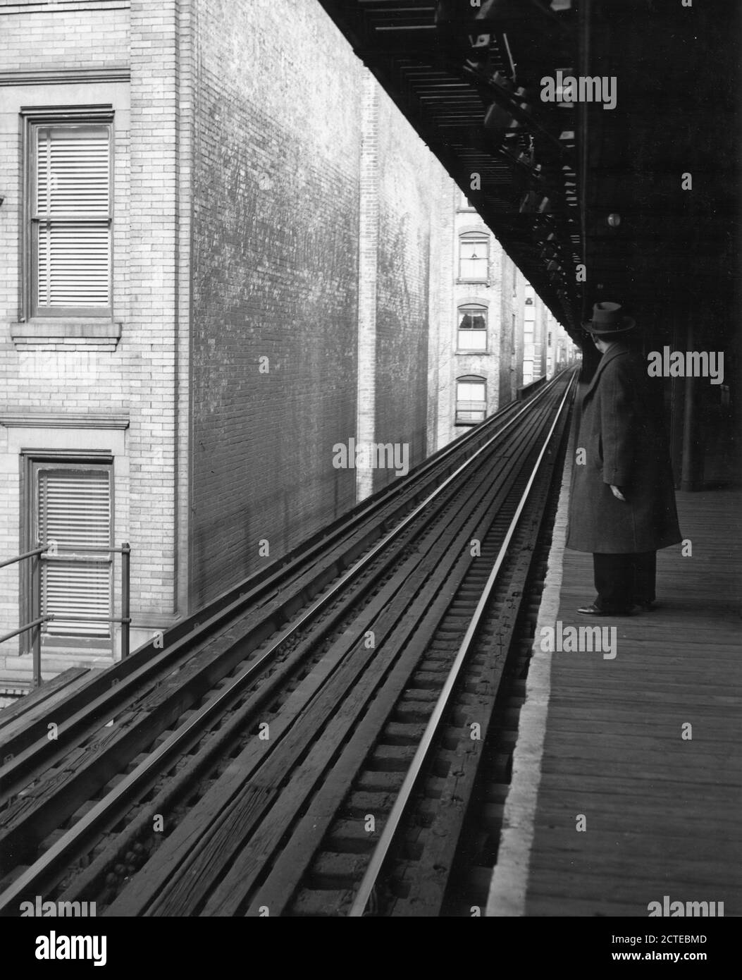 Vista di un passeggero solo in attesa su una piattaforma ferroviaria sopraelevata. In questa posizione del Bronx, i cingoli affollano strettamente gli edifici di affittuazione fino all'occhio può vedere, New York, NY, 1953. (Foto di United States Information Agency/RBM Vintage Images) Foto Stock