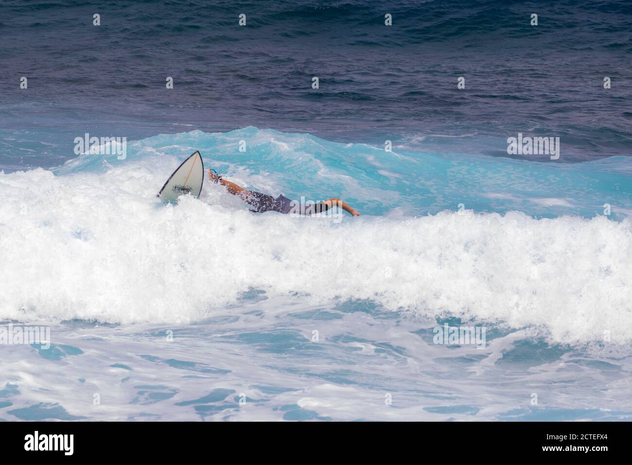 Capretto surfer che cade fuori dell'onda a Maui, Hawaii. Bambini hawaiani che pulono il surf. Wipeout dilettante del surfer. Surfista in camicia grigia cade dalla tavola da surf. Foto Stock