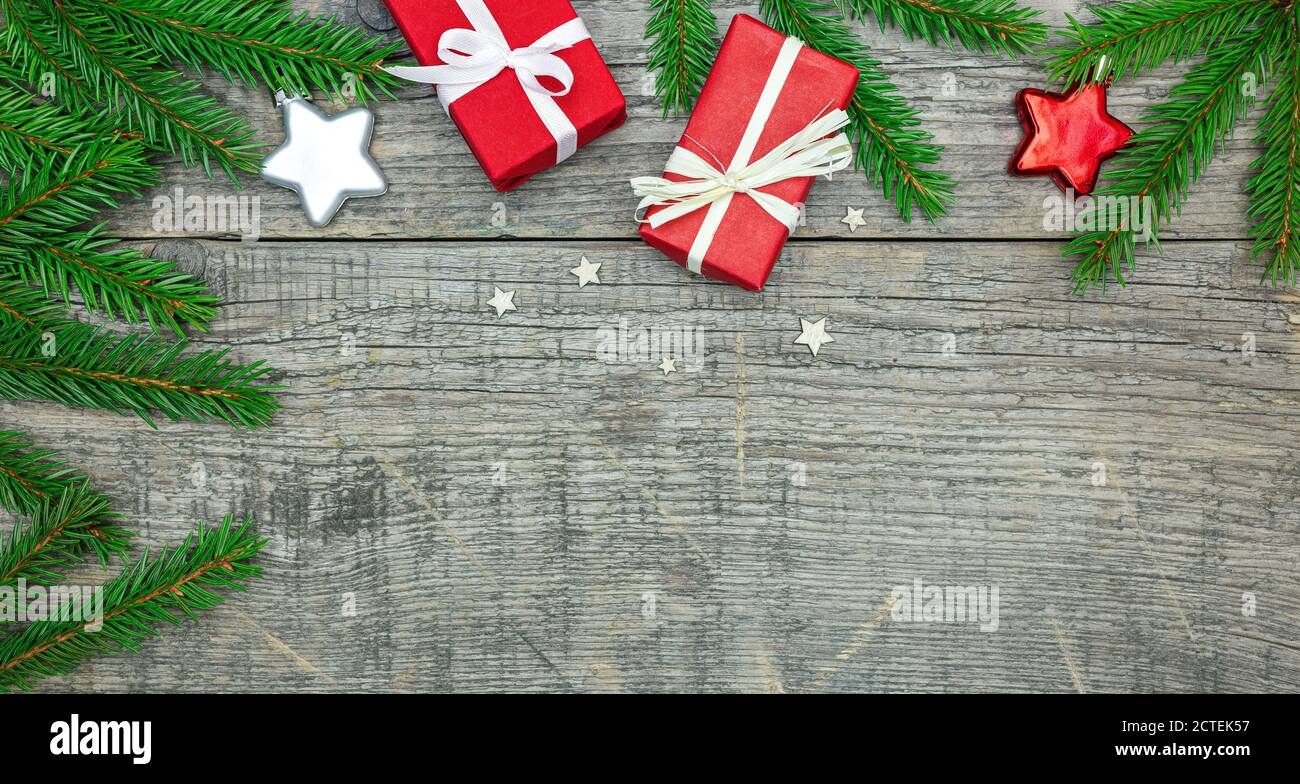 tavole di legno grigio decorate con rami di abete verde, stelle di vetro e piccole scatole regalo di carta rossa. sfondo festivo con decorazioni di nuovo anno Foto Stock