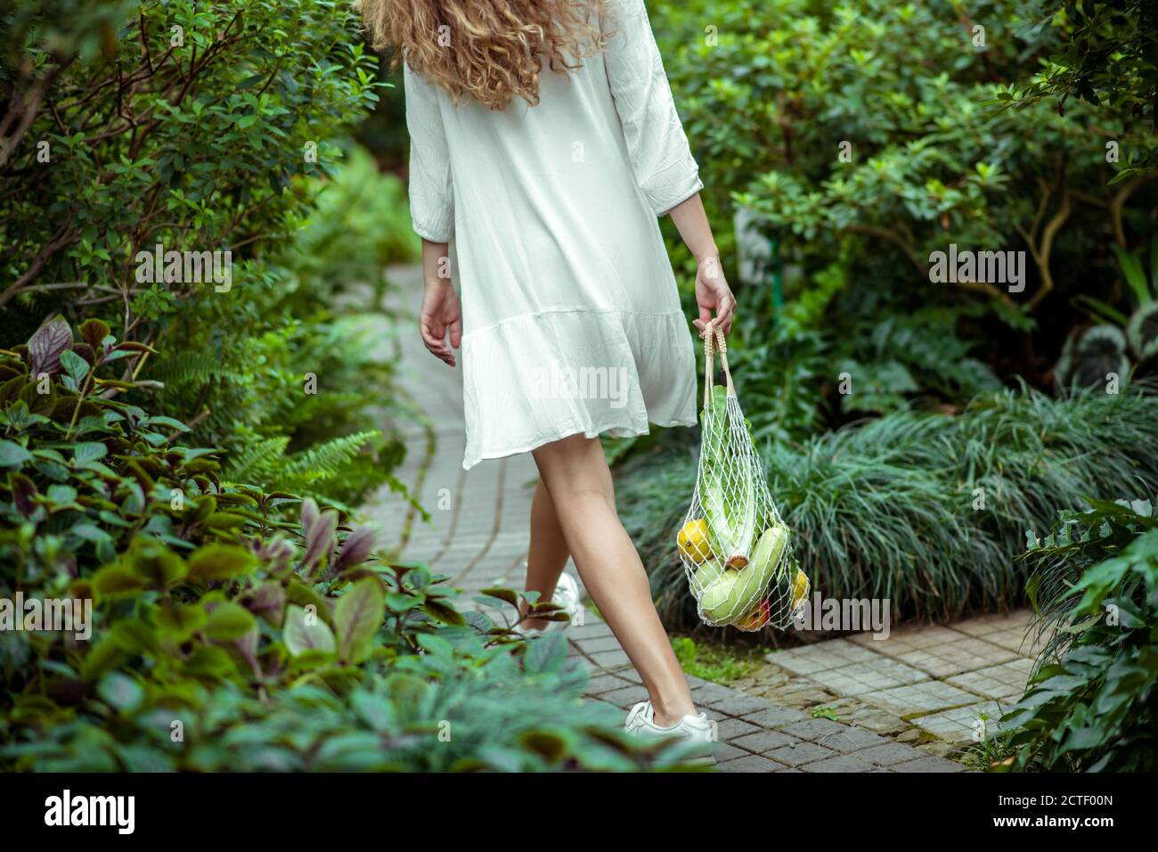 Donna in abito bianco Waling e borse da trasporto con diversi verdure Foto Stock