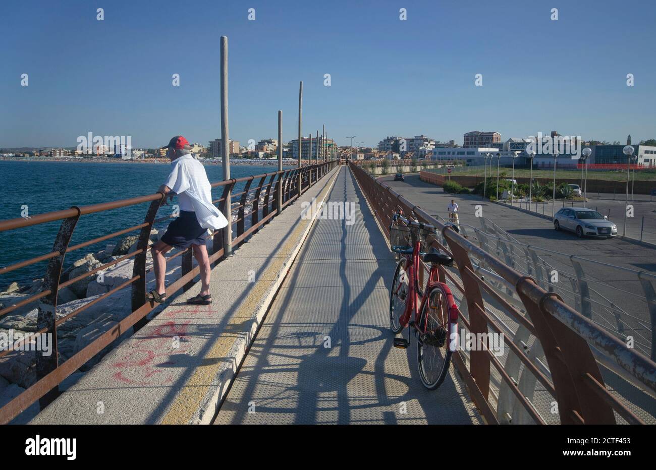 uomo anziano dopo aver parcheggiato la bicicletta lungo il molo della città si rilassa guardando la vista Foto Stock