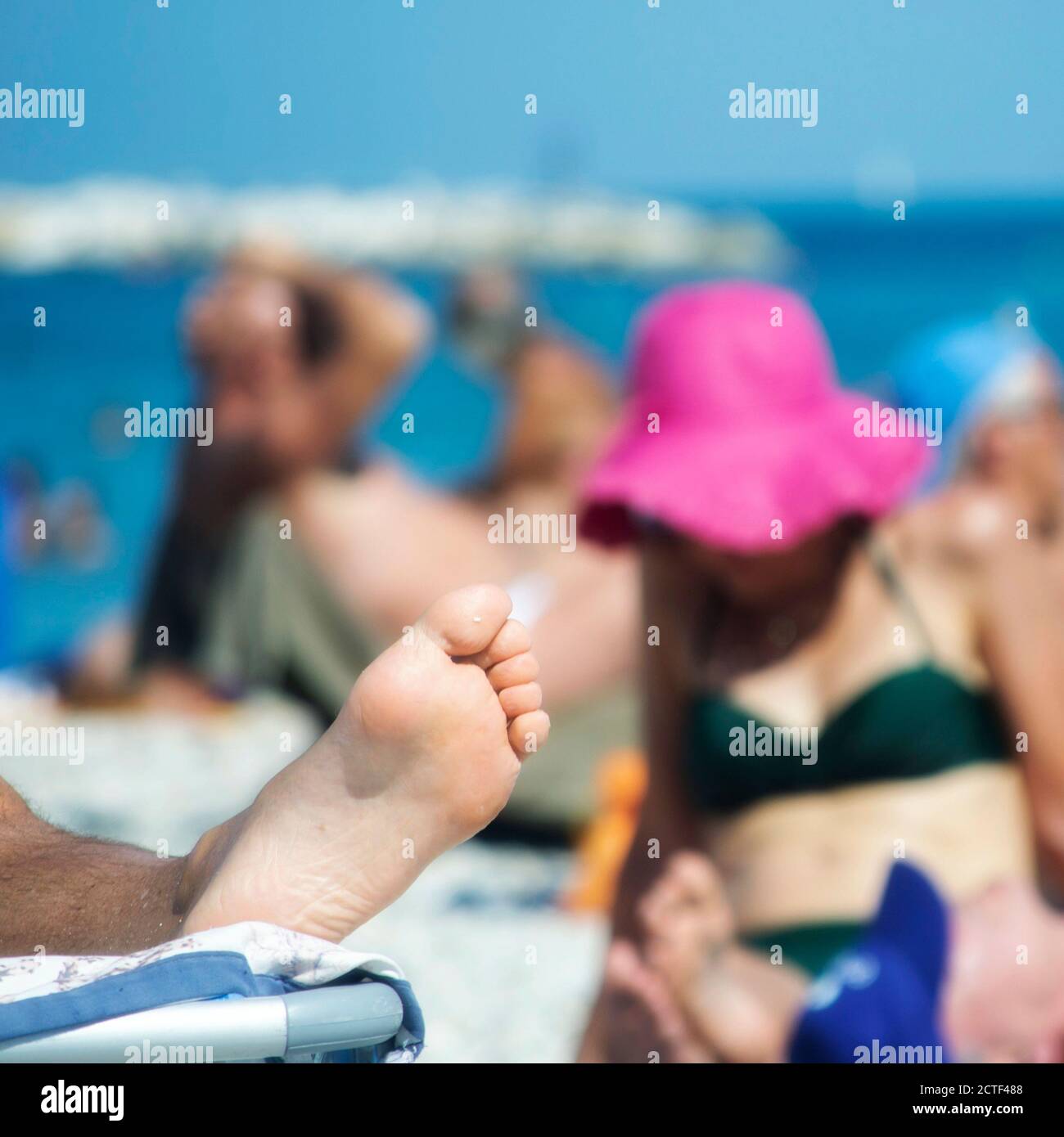 vista di una spiaggia libera lungo il mare adriatico a metà estate affollata di persone, con un piede di turista su una sedia da spiaggia in primo piano Foto Stock
