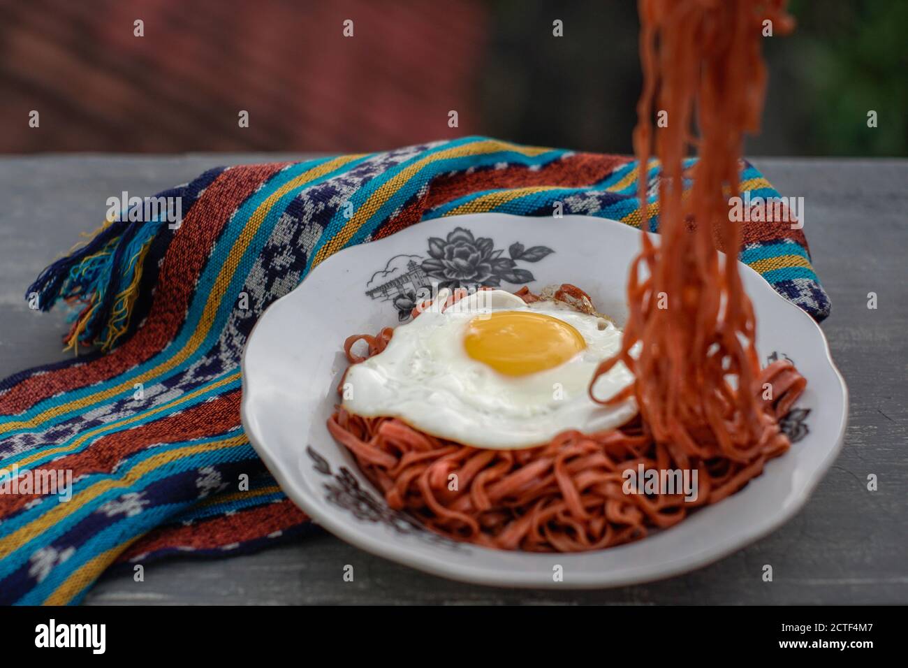 I tagliatelle fritte vengono gustati con uova fritte su un Piatto con un tipico ornamento di stoffa etnica Indonesiana Foto Stock