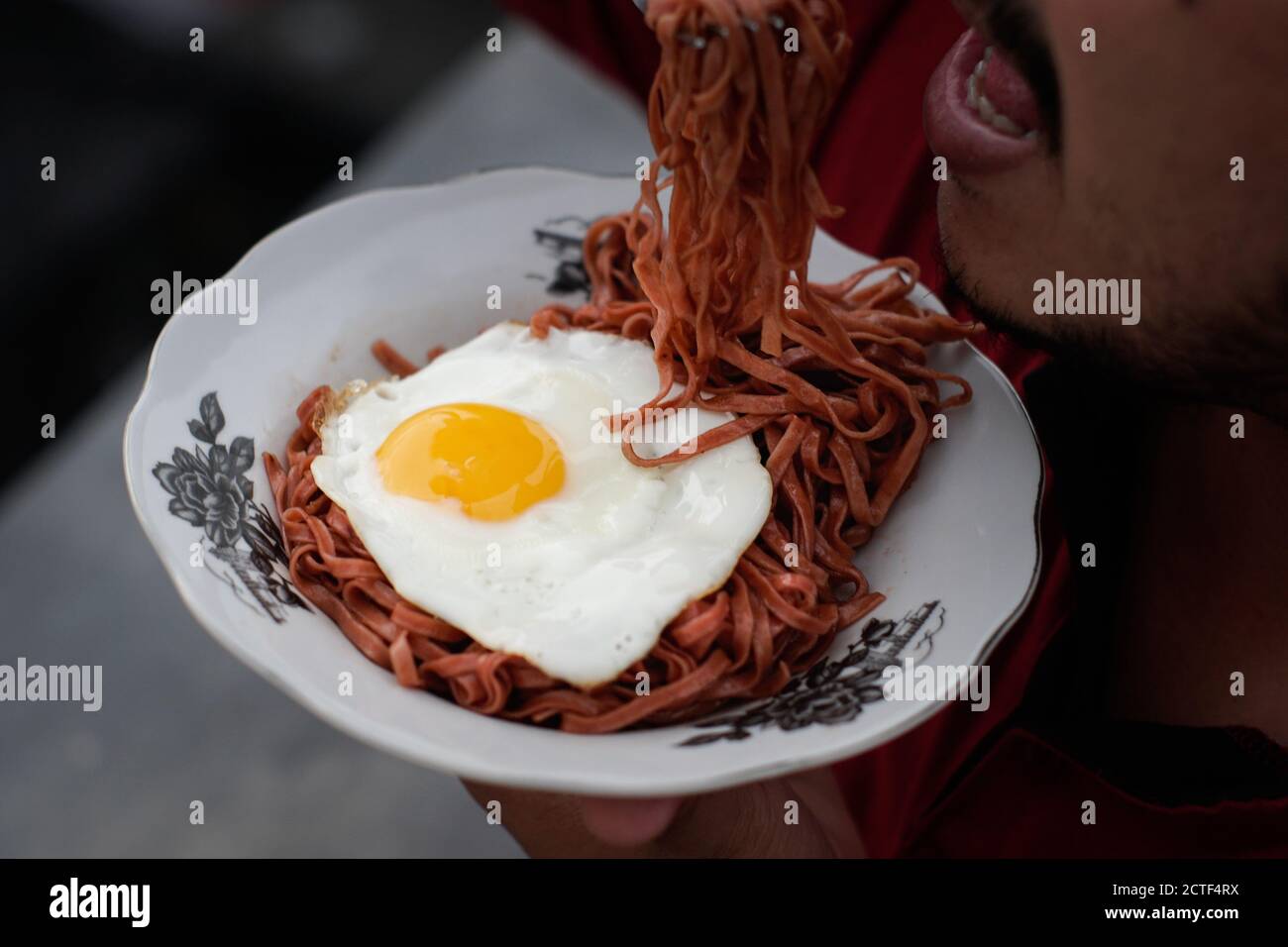 I tagliatelle fritte vengono gustati con uova fritte su un Piatto con un tipico ornamento di stoffa etnica Indonesiana Foto Stock