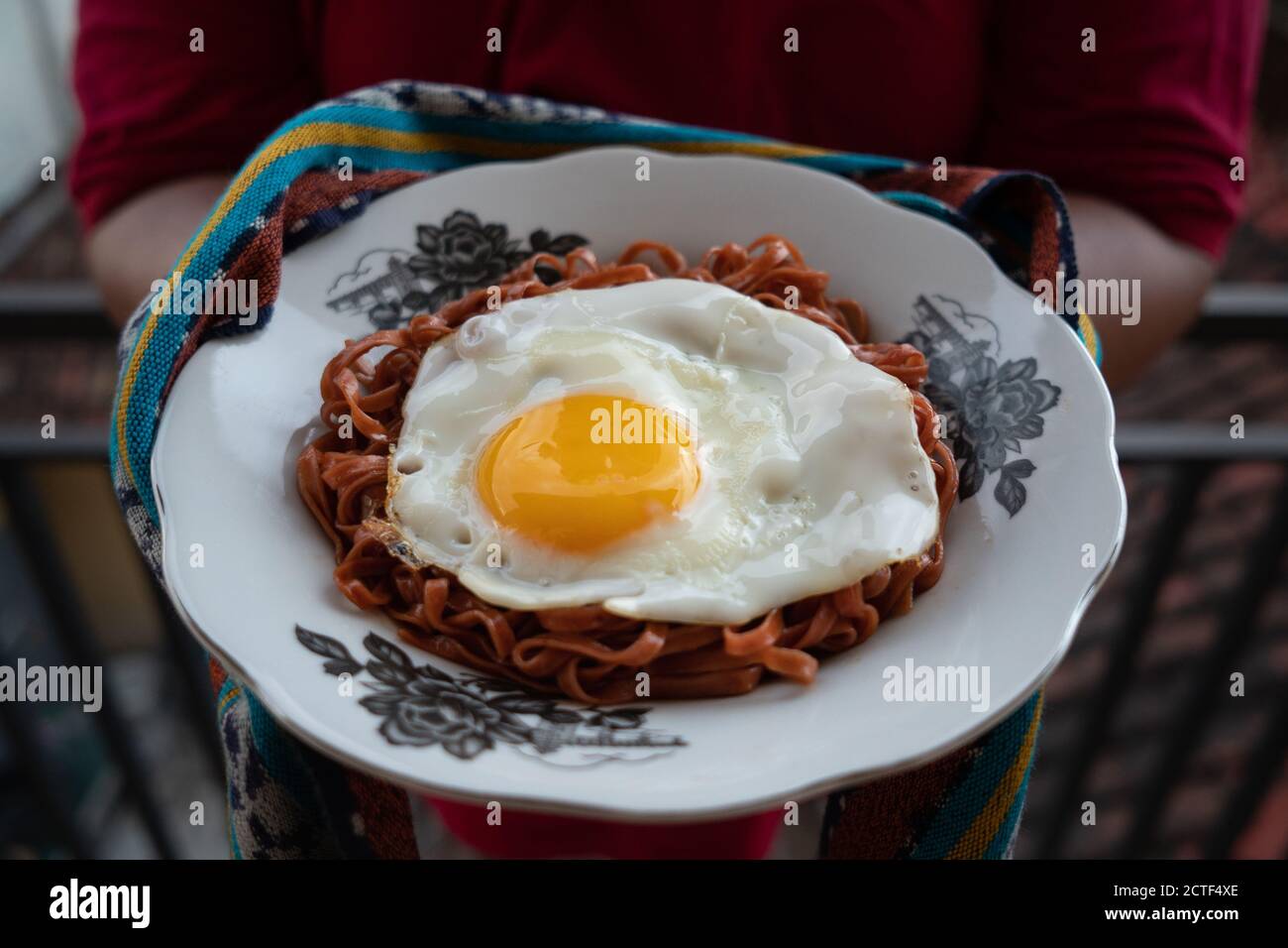 I tagliatelle fritte vengono gustati con uova fritte su un Piatto con un tipico ornamento di stoffa etnica Indonesiana Foto Stock