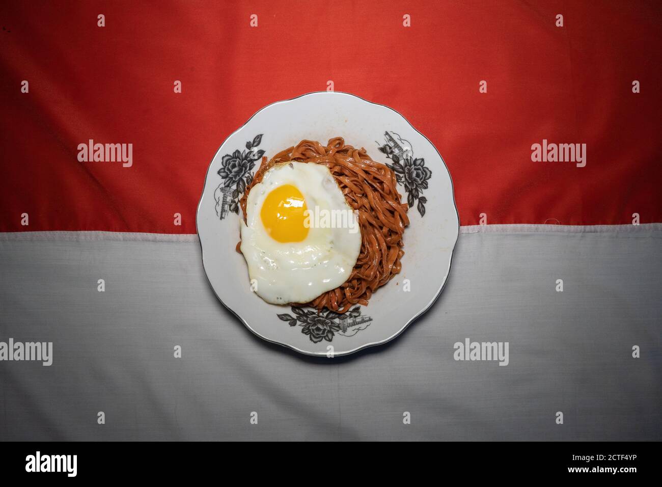 I tagliatelle fritte vengono gustati con uova fritte su un Piatto con un tipico ornamento di stoffa etnica Indonesiana Foto Stock