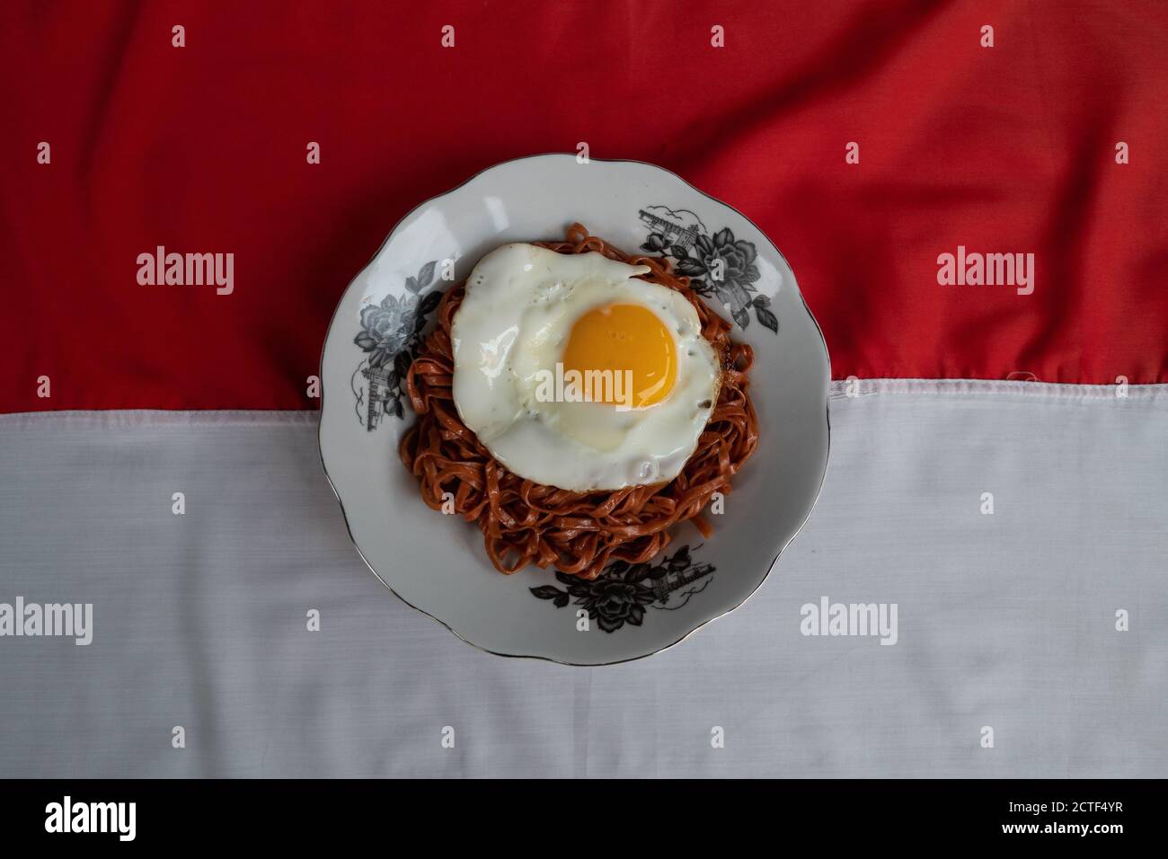 I tagliatelle fritte vengono gustati con uova fritte su un Piatto con un tipico ornamento di stoffa etnica Indonesiana Foto Stock