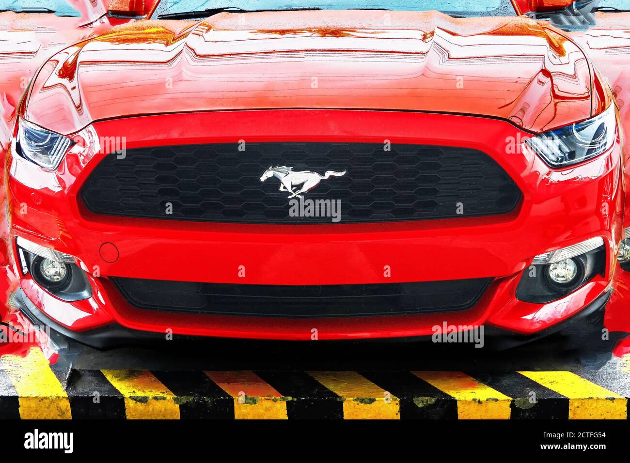 Vista isolata di un'auto sportiva Ford Mustang di colore rosso, fotografata dall'angolo anteriore basso, ritoccata ad un collage, con simbolo di cavallo prominente Foto Stock