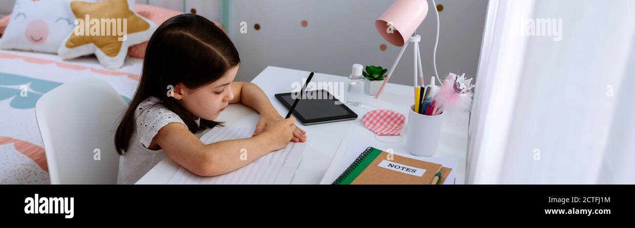 Ragazza che studia a casa con maschera sul tavolo Foto Stock