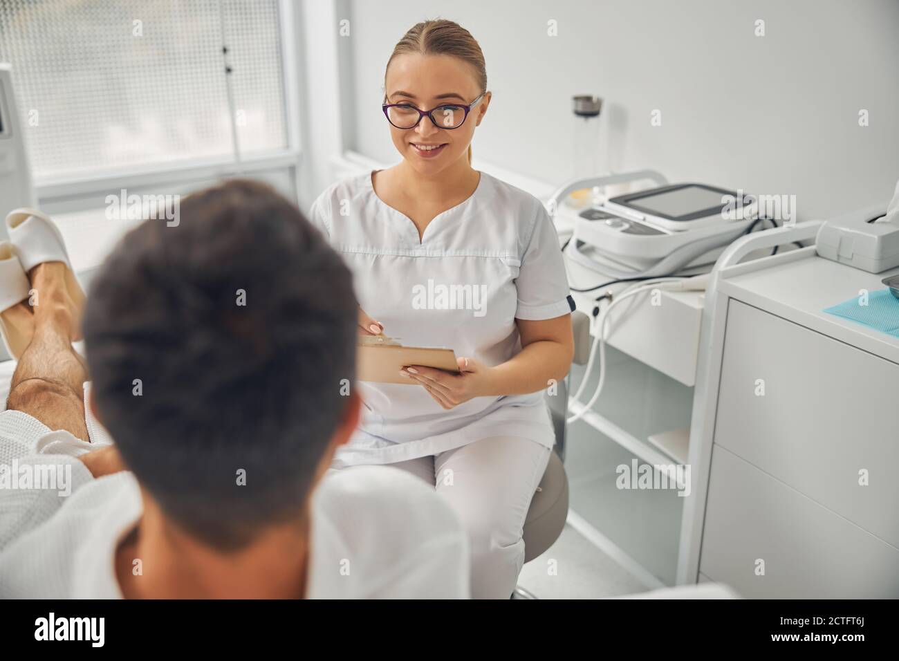 Bella donna cosmetologa che guarda paziente maschile e sorridente mentre tenendo gli appunti Foto Stock