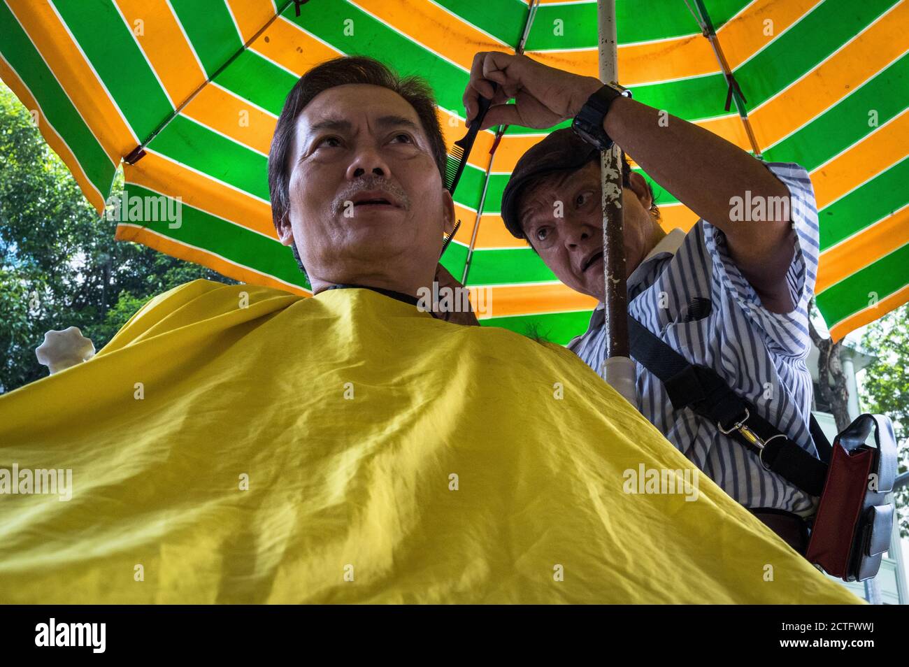 Uomo che ottiene un taglio di capelli all'aperto, ho Chi Minh City, Vietnam Foto Stock