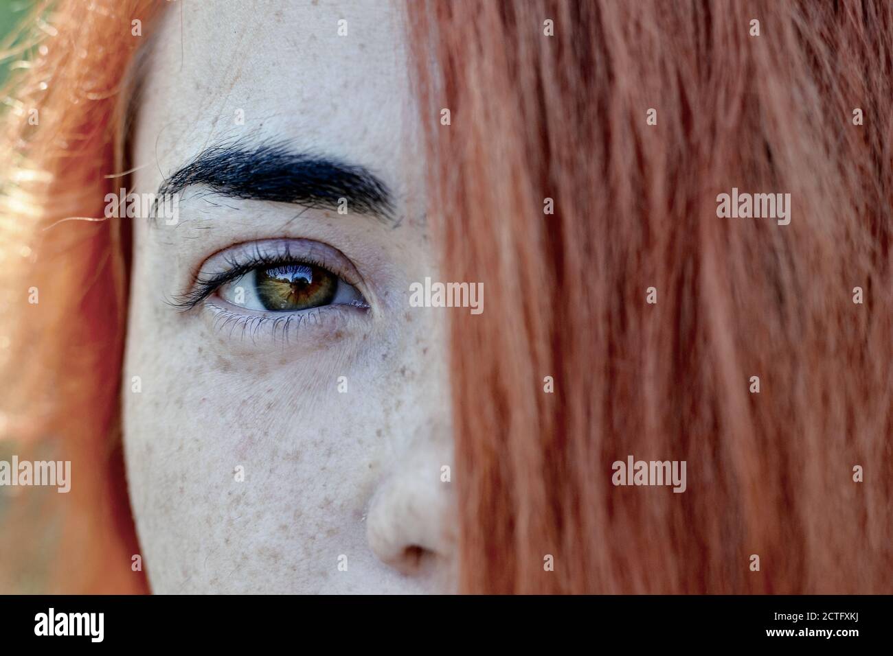 Primo piano ritratto di una ragazza donna capelli rossi con frettole. Ritratto di una ragazza all'aperto alla luce del sole. I capelli coprono metà del viso. Foto Stock