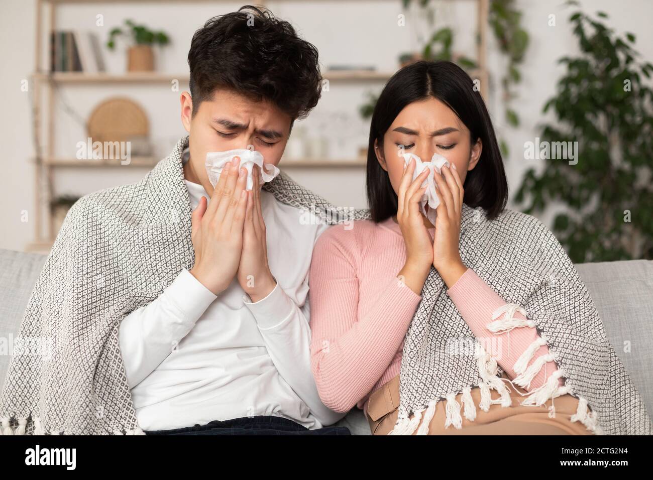 Ammalato i coniugi giapponesi che soffiano il naso seduto sul divano a casa Foto Stock