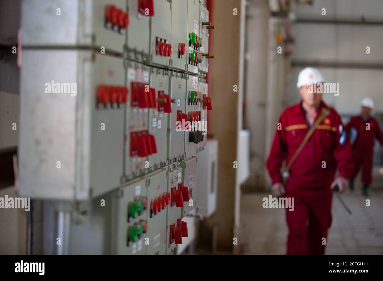 Quadro di comando remoto per apparecchiature elettriche e di elaborazione (console). Raffineria di petrolio e impianto di lavorazione del gas. Operai di raffineria offuscati in casco bianco. Foto Stock