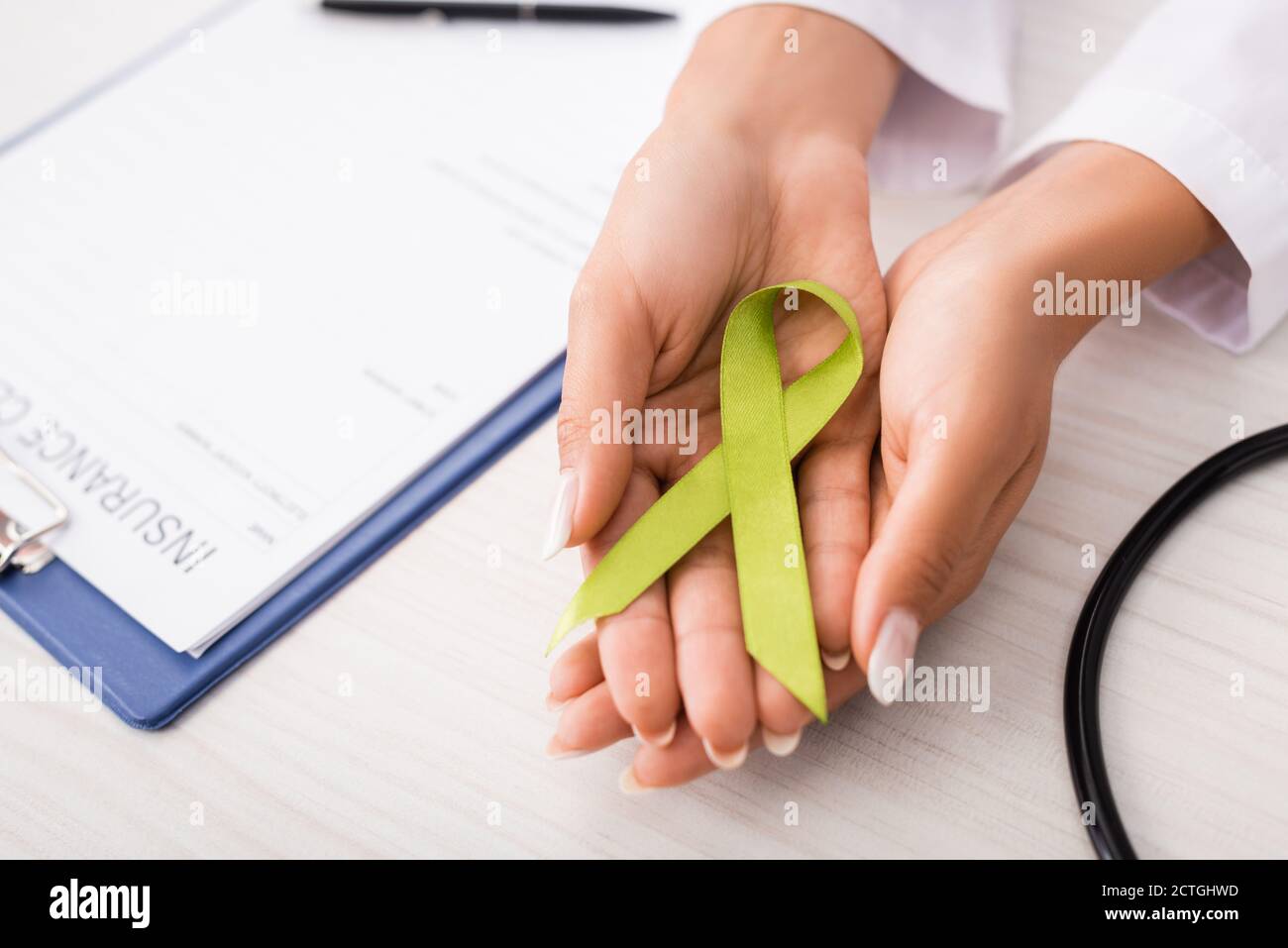 vista dall'alto del medico che tiene il nastro di consapevolezza verde vicino alla forma di reclamo di assicurazione, concetto di salute mentale Foto Stock