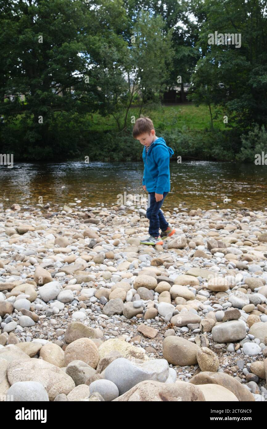 Ragazzo di quattro anni che gioca con pietre sul lato del fiume Wharfe in Ilkley West Yorkshire. Foto Stock