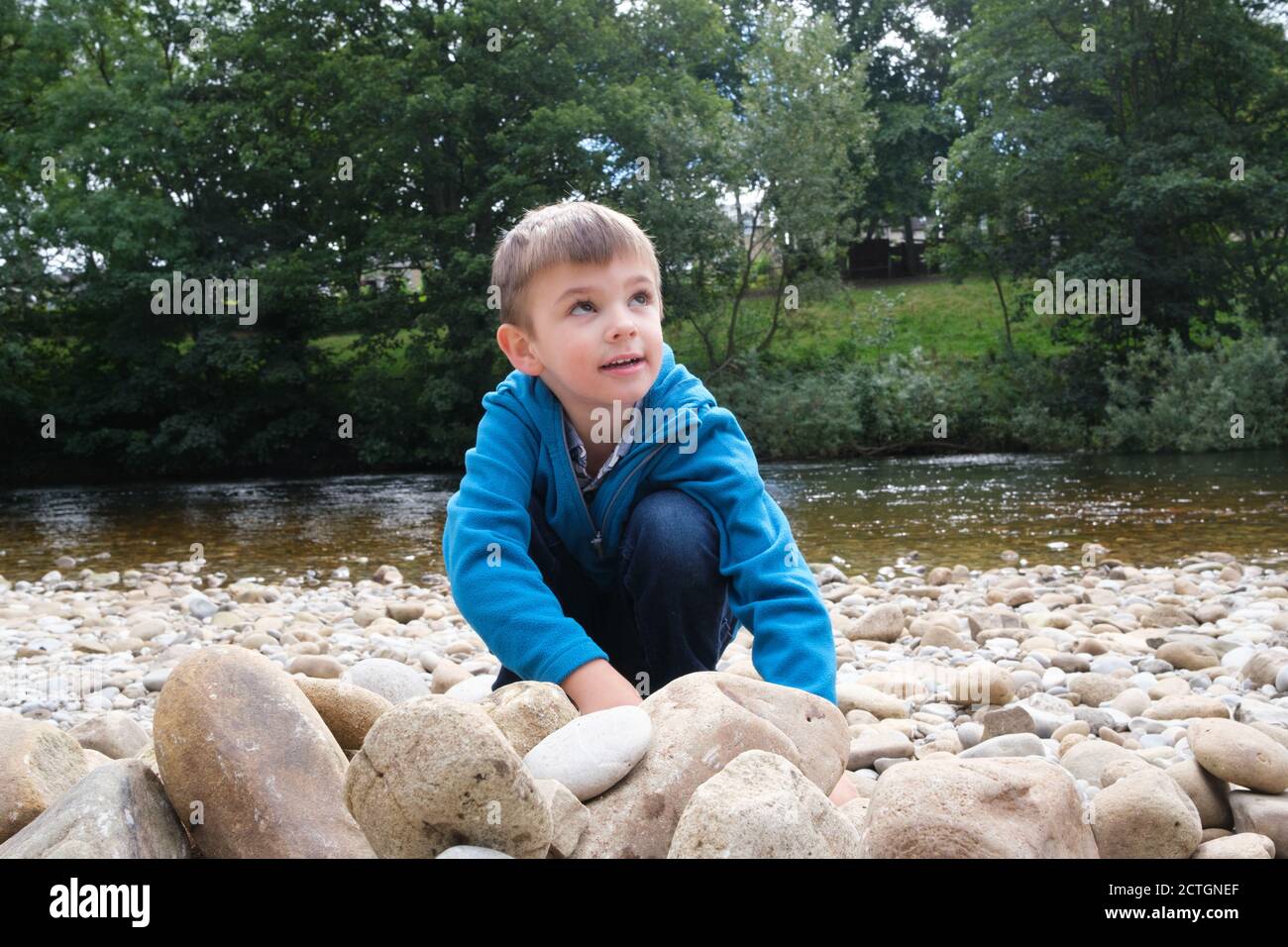 Ragazzo di quattro anni che gioca con pietre sul lato del fiume in Ilkley West Yorkshire. Foto Stock