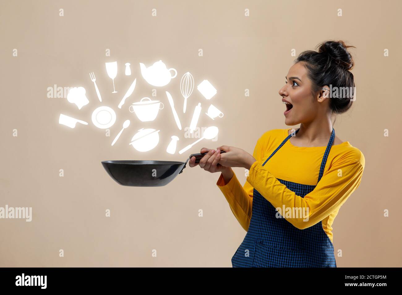 Donna che guarda gli oggetti essenziali della cucina con un wok in lei mano Foto Stock