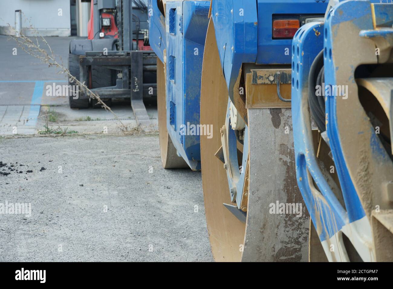 Attrezzature di ingegneria pesante, tra cui rullo di separazione del tamburo dell'asfaltatrice blu e impilatore per carrelli elevatori rosso e nero parcheggiato durante i giorni del fine settimana vicino alla costruzione. Foto Stock