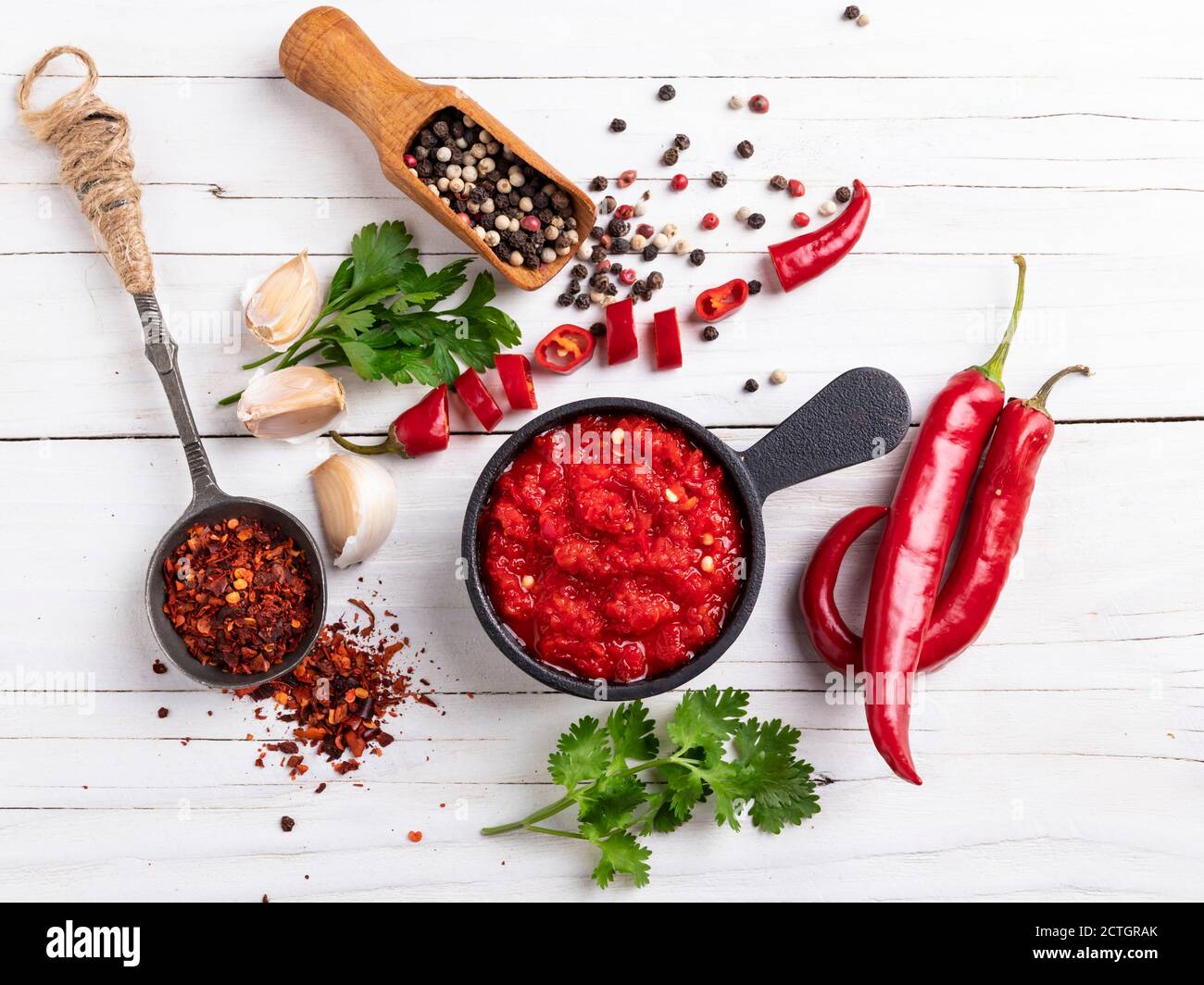 salsa rossa piccante al pepe, ingredienti, spezie su una superficie di legno bianco Foto Stock