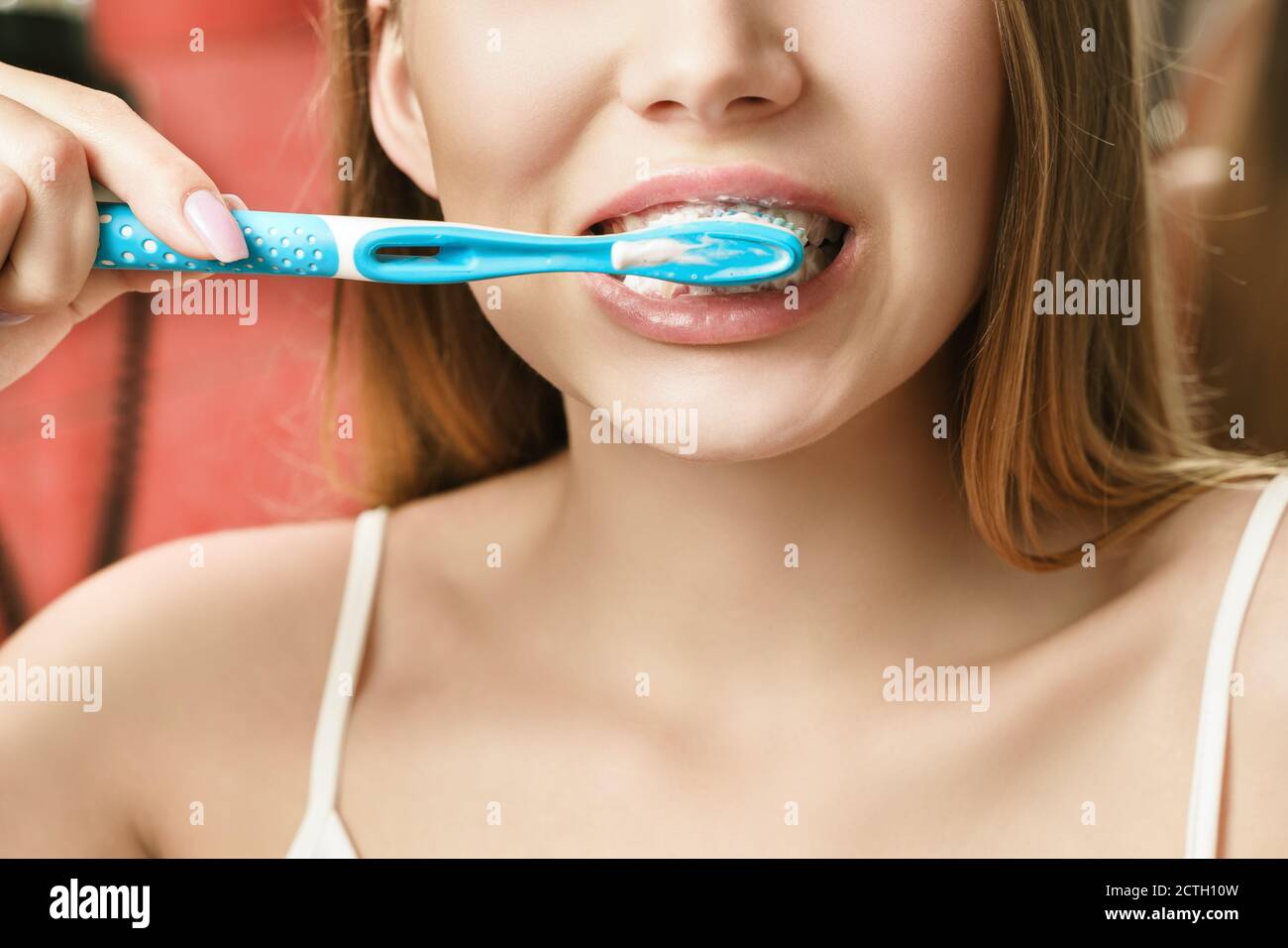 Una giovane donna sta spazzolando i denti in bagno. Riflessione nello specchio Foto Stock