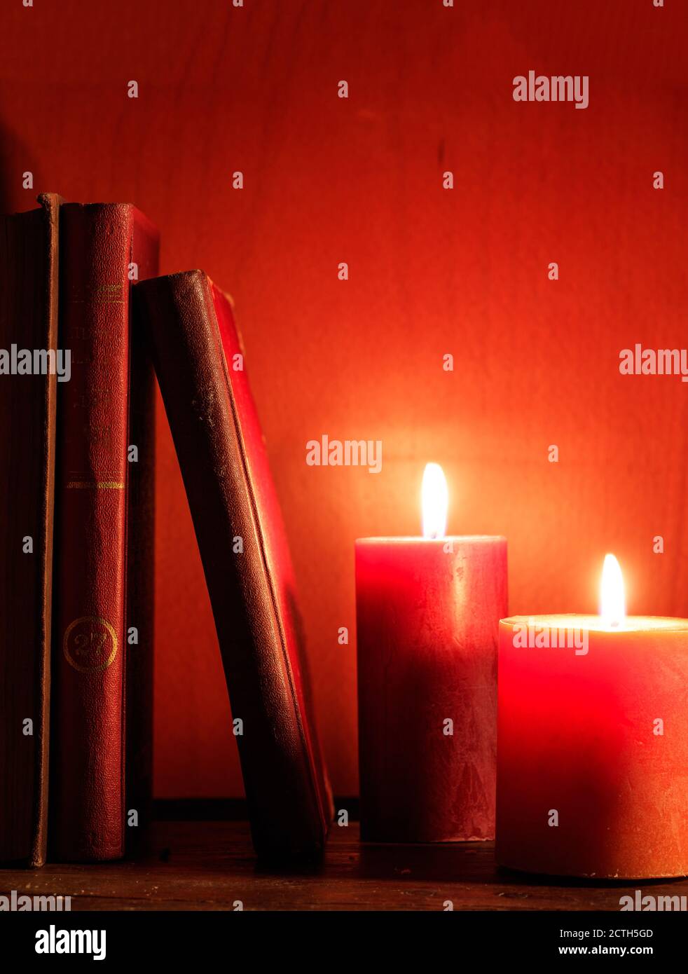 Libri antichi e candele illuminate su un tavolo di legno, candele di colore rosso sfondo, verticale Foto Stock