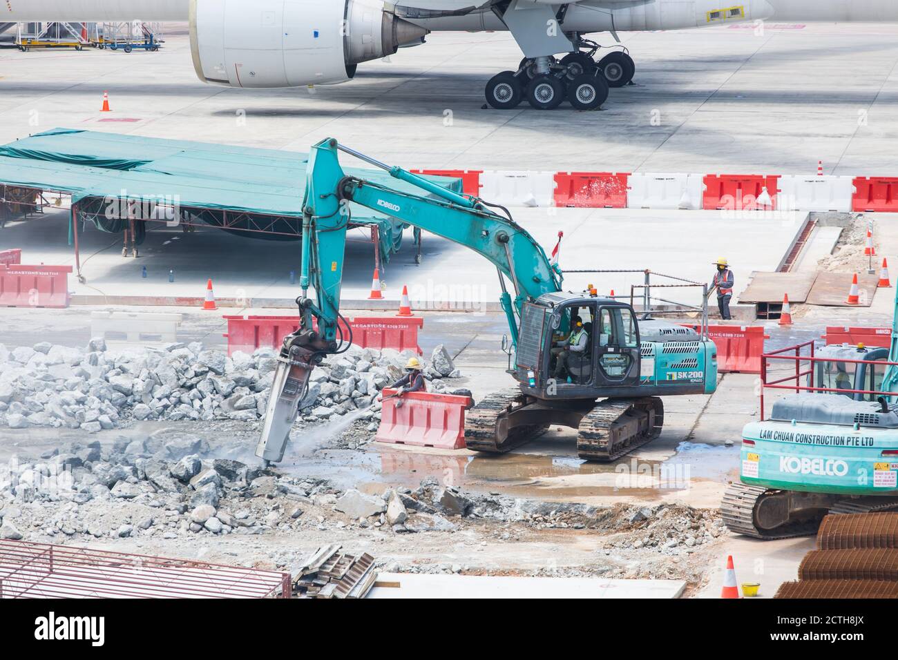 Grembiule dell'aeroporto in fase di ricostruzione, un lavoratore spruzzerà getti d'acqua sul trapano dell'escavatore per raffreddare la temperatura riscaldata. Foto Stock