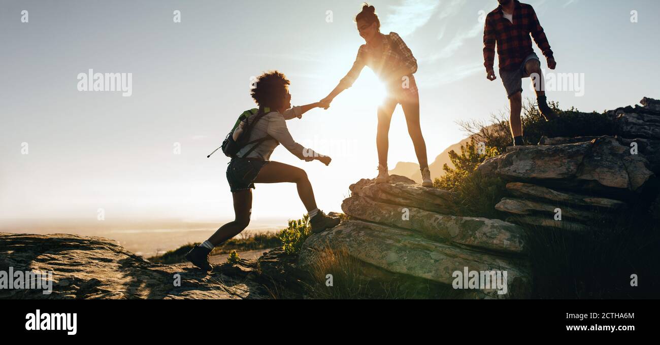 Donna che aiuta l'amico a salire sulla roccia durante le escursioni. Lavoro di squadra di due donne escursionisti che si aiutano l'un l'altro in cima alla montagna arrampicata. Foto Stock