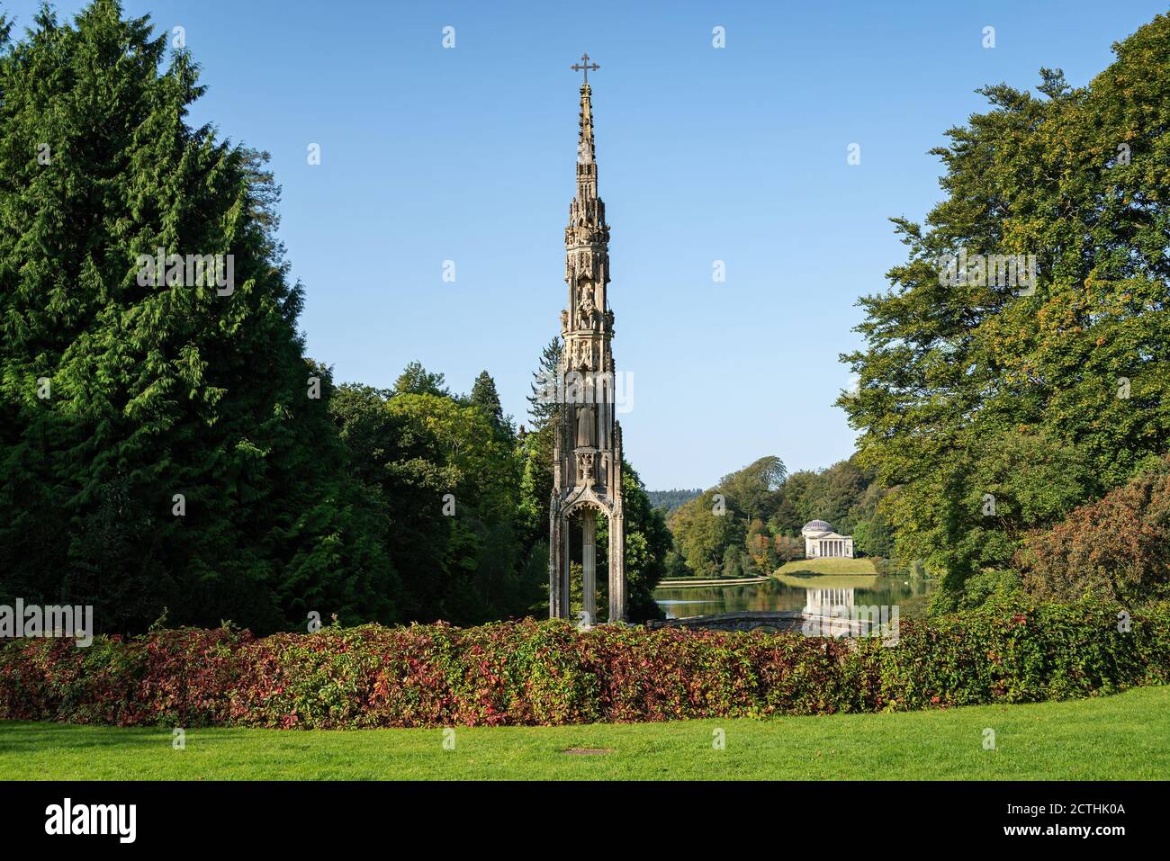 Bristol monumento a croce alta con siepe in primo piano e il Pantheon a attraversare il lago in lontananza con cielo blu chiaro. Giardini Stourhead. Foto Stock