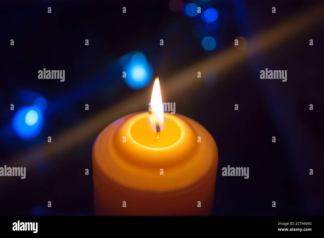 Una candela arancione acceso su uno sfondo scuro con luci blu - un Natale Capodanno divinazione mistico esoterico amore amore umore. Foto orizzontale, laterale, messa a fuoco o messa a fuoco. Foto Stock