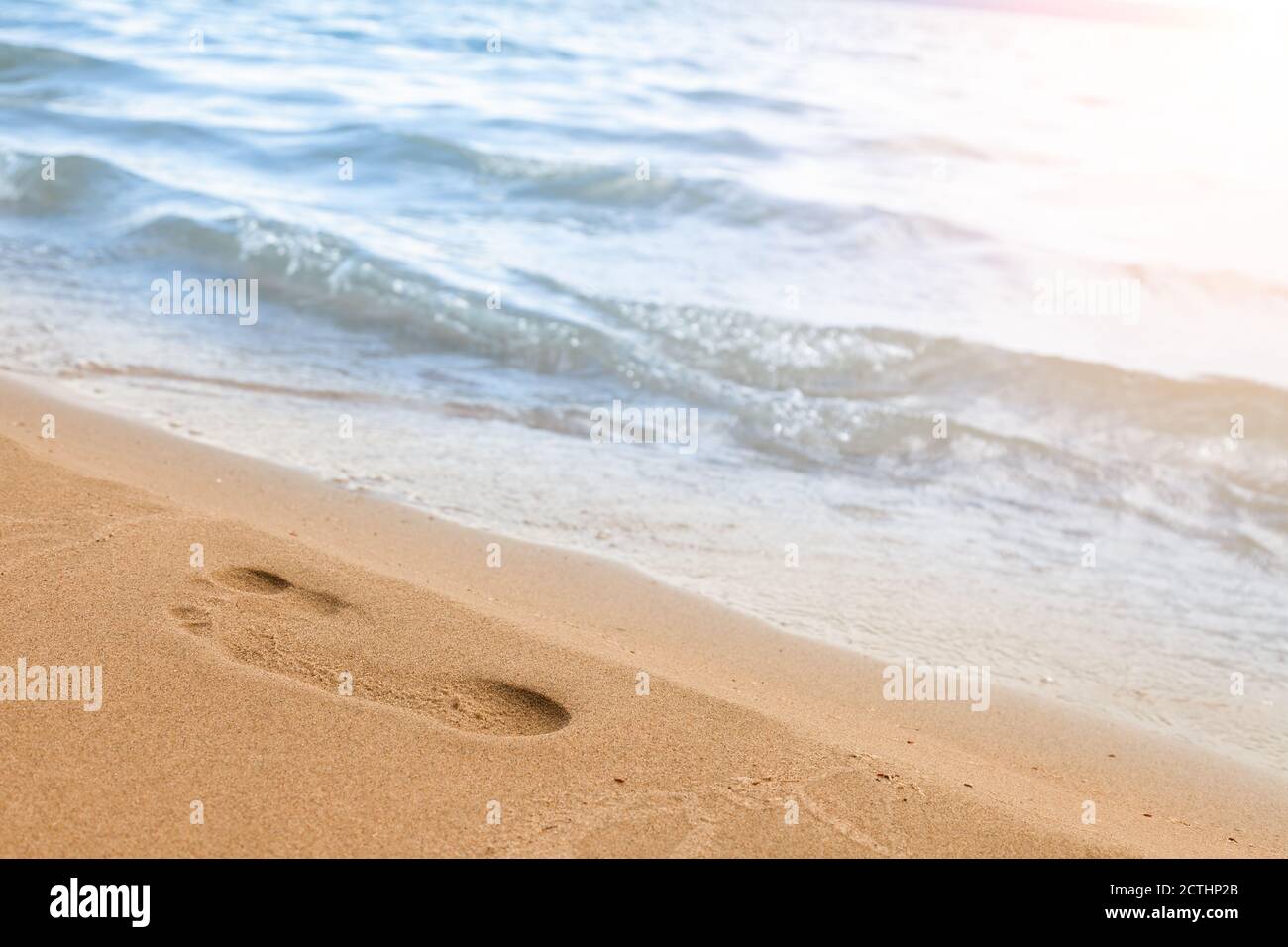 Primo piano della spiaggia con l'impronta di un uomo sulla sabbia gialla lungo la linea dell'onda blu del mare in una giornata estiva di sole. Sfondo per l'annuncio Foto Stock