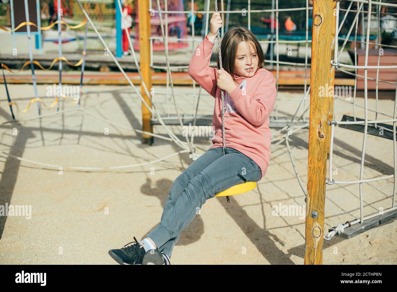 Carina caucasica ragazza 7-8 anni in una felpa rosa e pantaloni grigi sul parco giochi nel parco cittadino. Attività all'aperto, stile di vita, leisù per bambini Foto Stock
