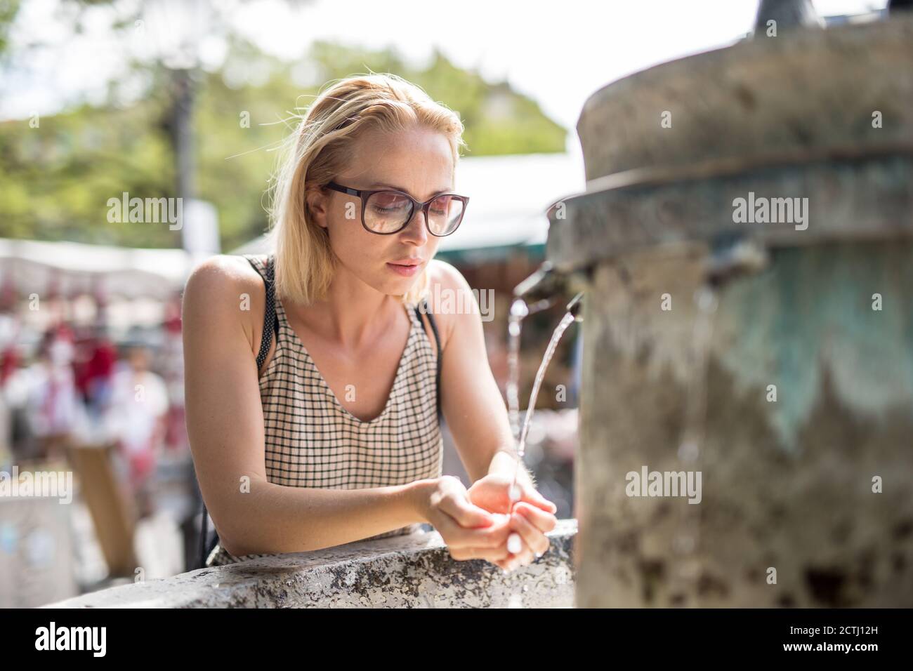 Assetata giovane donna cucasual che beve acqua dalla città pubblica fontana in una calda giornata estiva Foto Stock