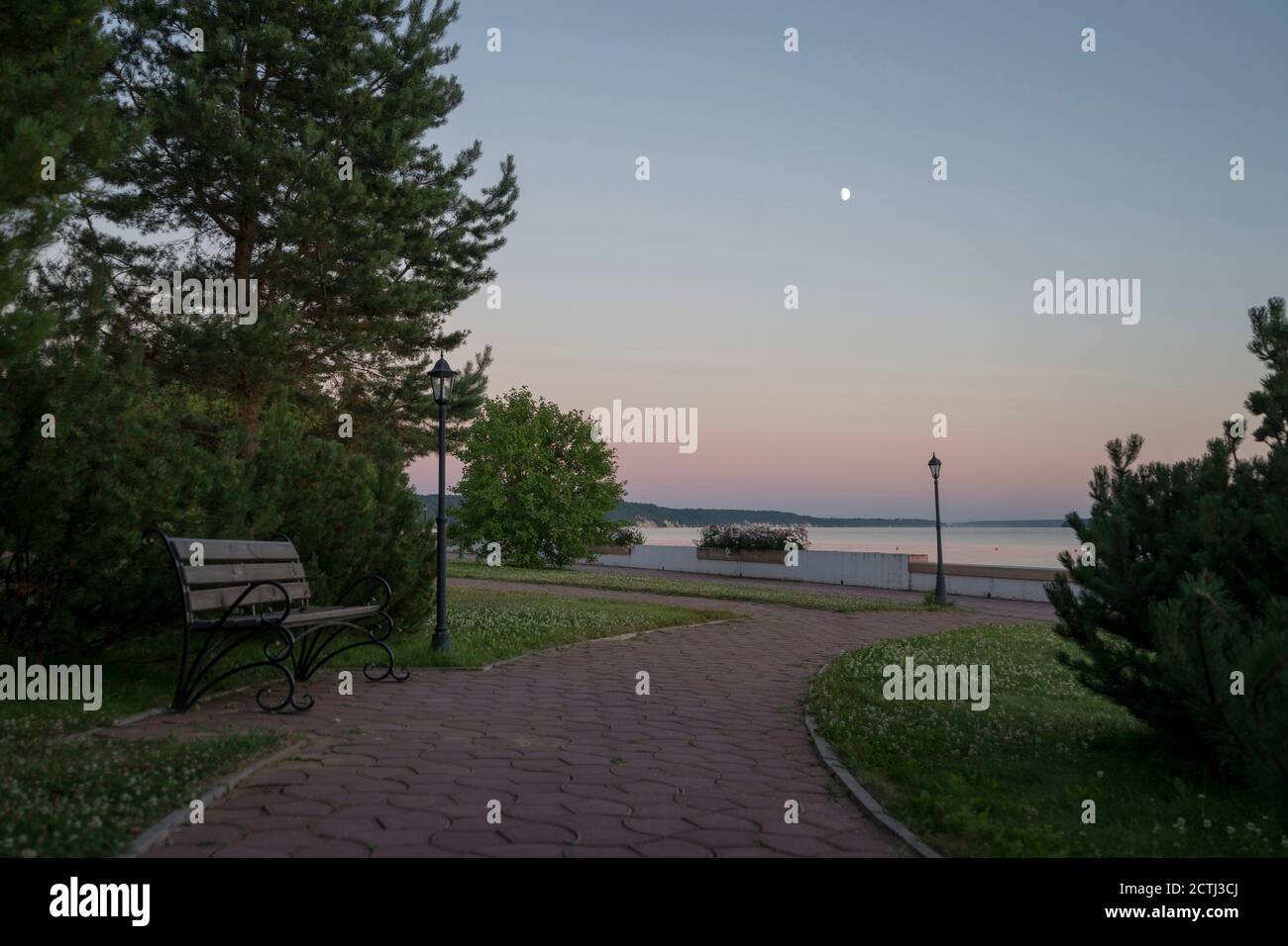 Comodo fiume o riva del lago con pavimentazione e panca al crepuscolo Foto Stock