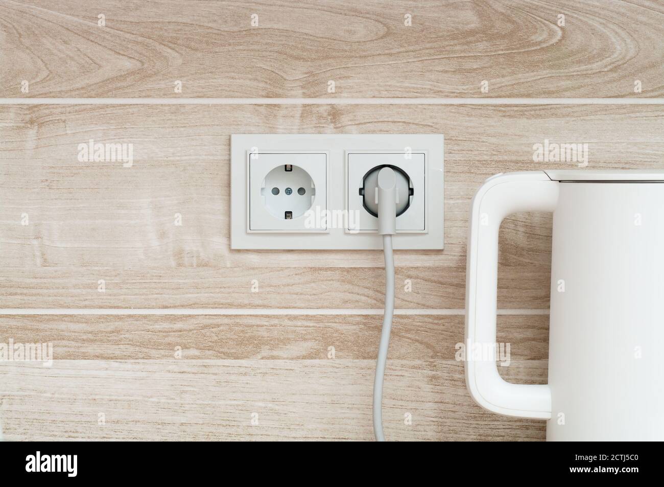 bollitore elettrico bianco collegato a una presa di corrente su muro in una cucina Foto Stock