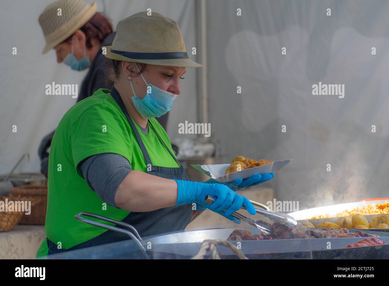 Donna che serve cibo con maschera e guanti in un festival del mercato alimentare di strada, ottobre Fest Foto Stock