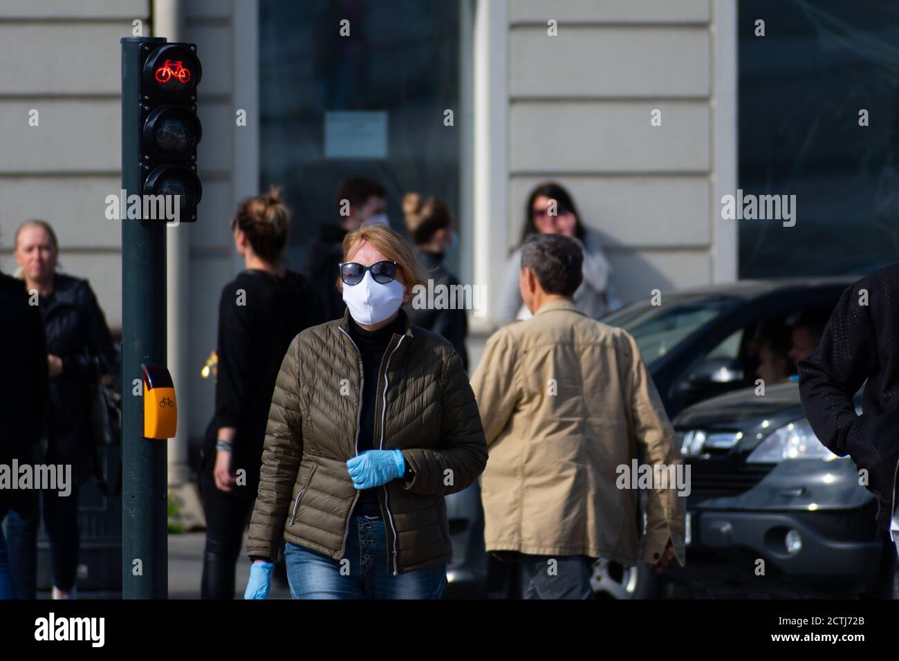 Donna con maschera e guanti che cammina nel centro della città vicino al semaforo rosso durante l'epidemia di Covid o Coronavirus, maschere obbligatorie Foto Stock