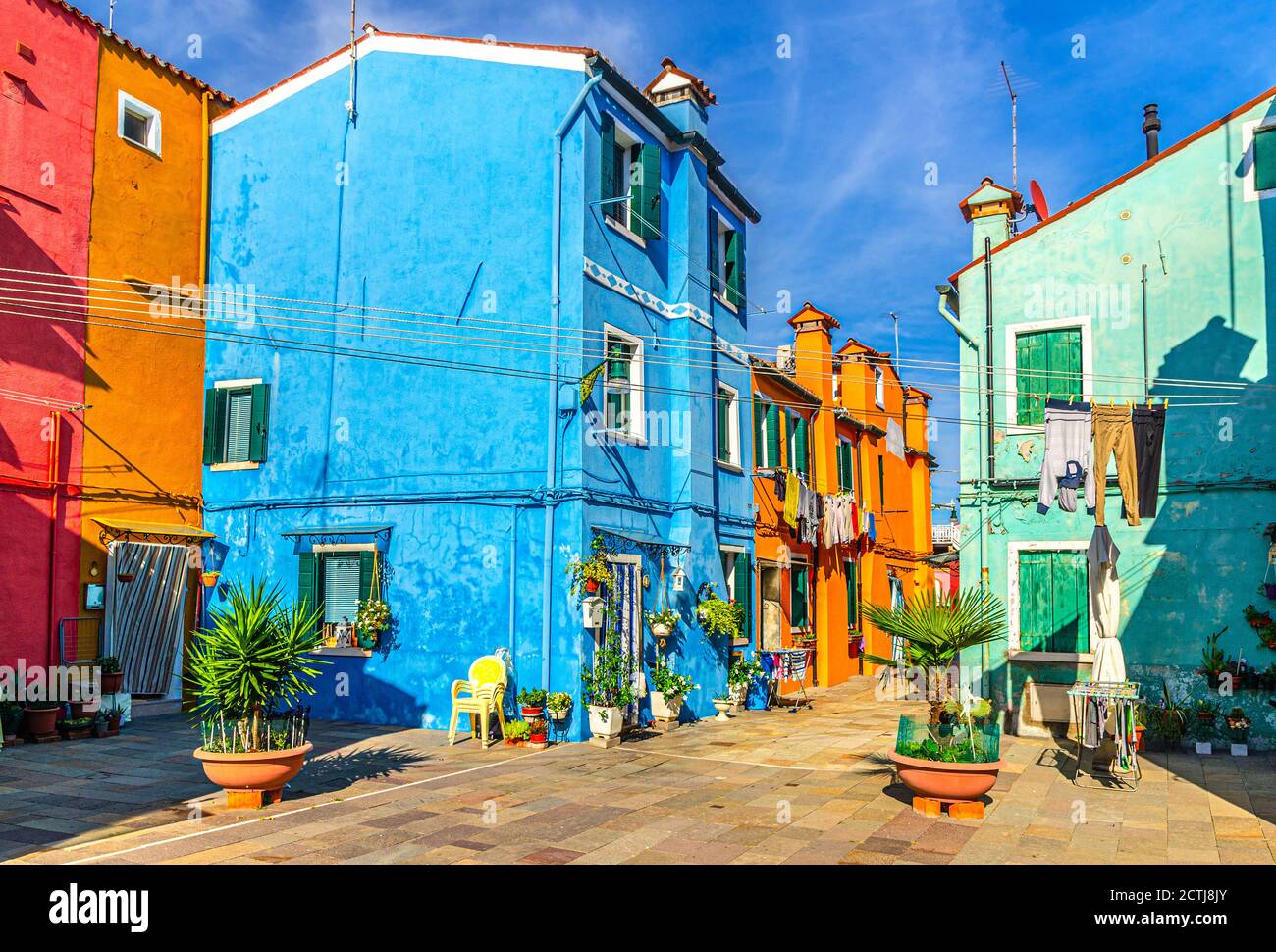 Case colorate dell'isola di Burano. Edifici multicolore e fiori in pentole in piccola piazza, cielo blu su fondo in sole giornate estive, provincia di Venezia, Regione Veneto, Italia settentrionale. Burano cartolina Foto Stock