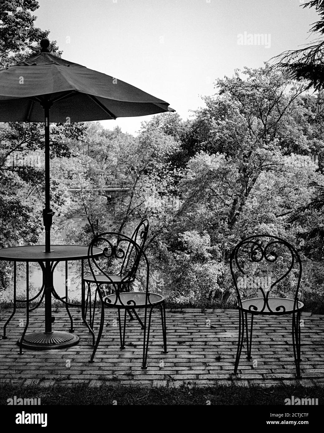 Tavolo esterno in metallo e sedie disposte come se fossero in uso sopra il fiume Concord. Più in profondità nel burrone luminoso un ponte è visibile attraverso l'acqua Foto Stock