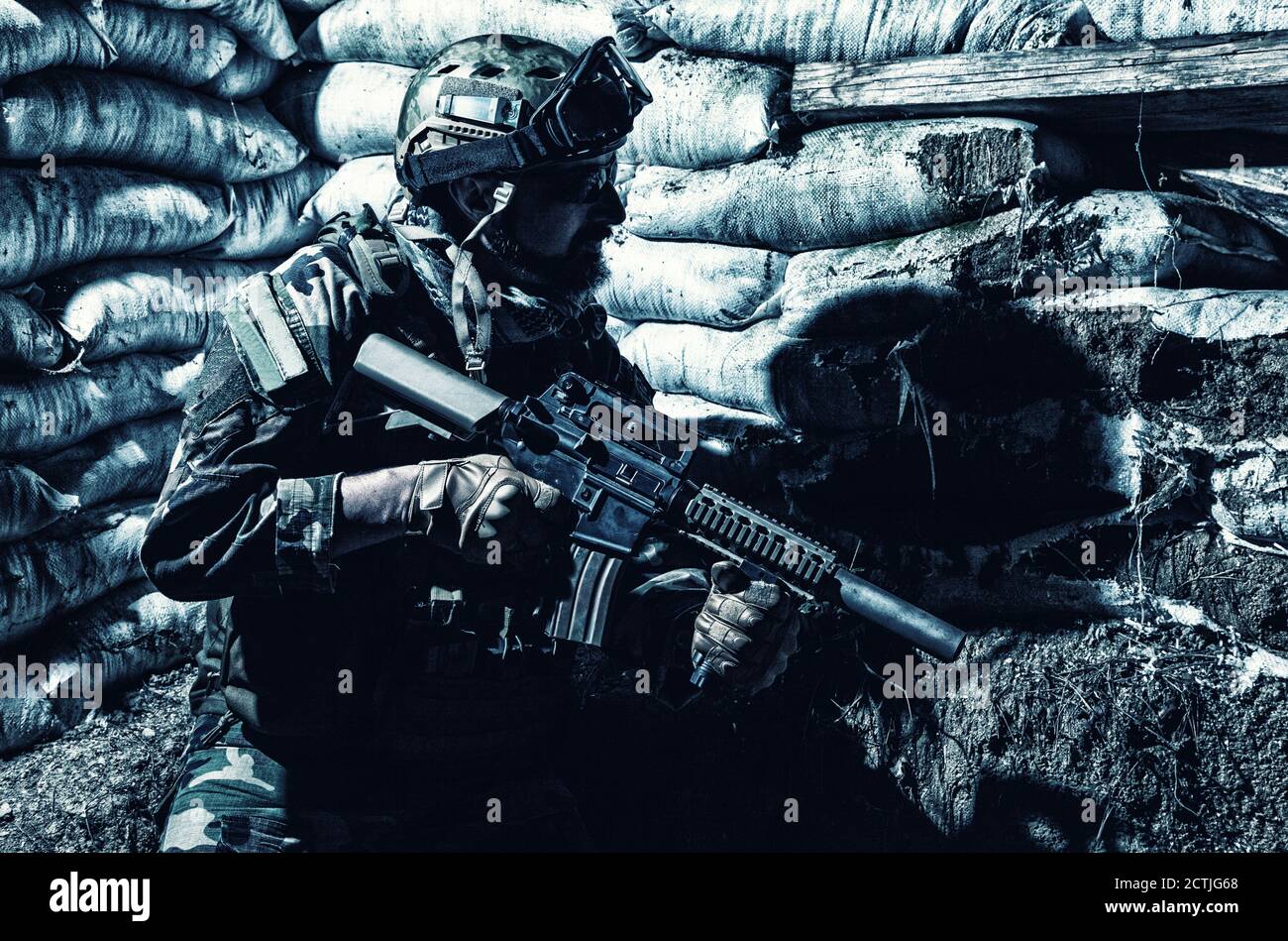 Caccia Navy SEALs, soldato dell'esercito in uniforme da combattimento,  occhiali e casco da battaglia a guardia notturna, seduto con fucile  d'assalto in trincea con borse di sabbia, guardando in buca, in attesa