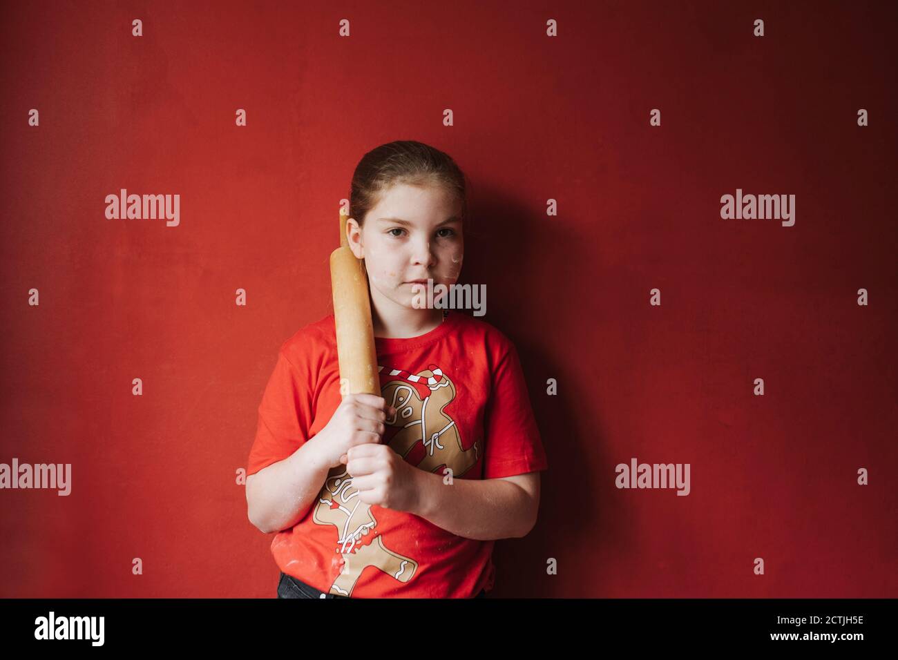 Ragazza in piedi e tenendo un perno di rotolamento di legno contro un parete rossa Foto Stock