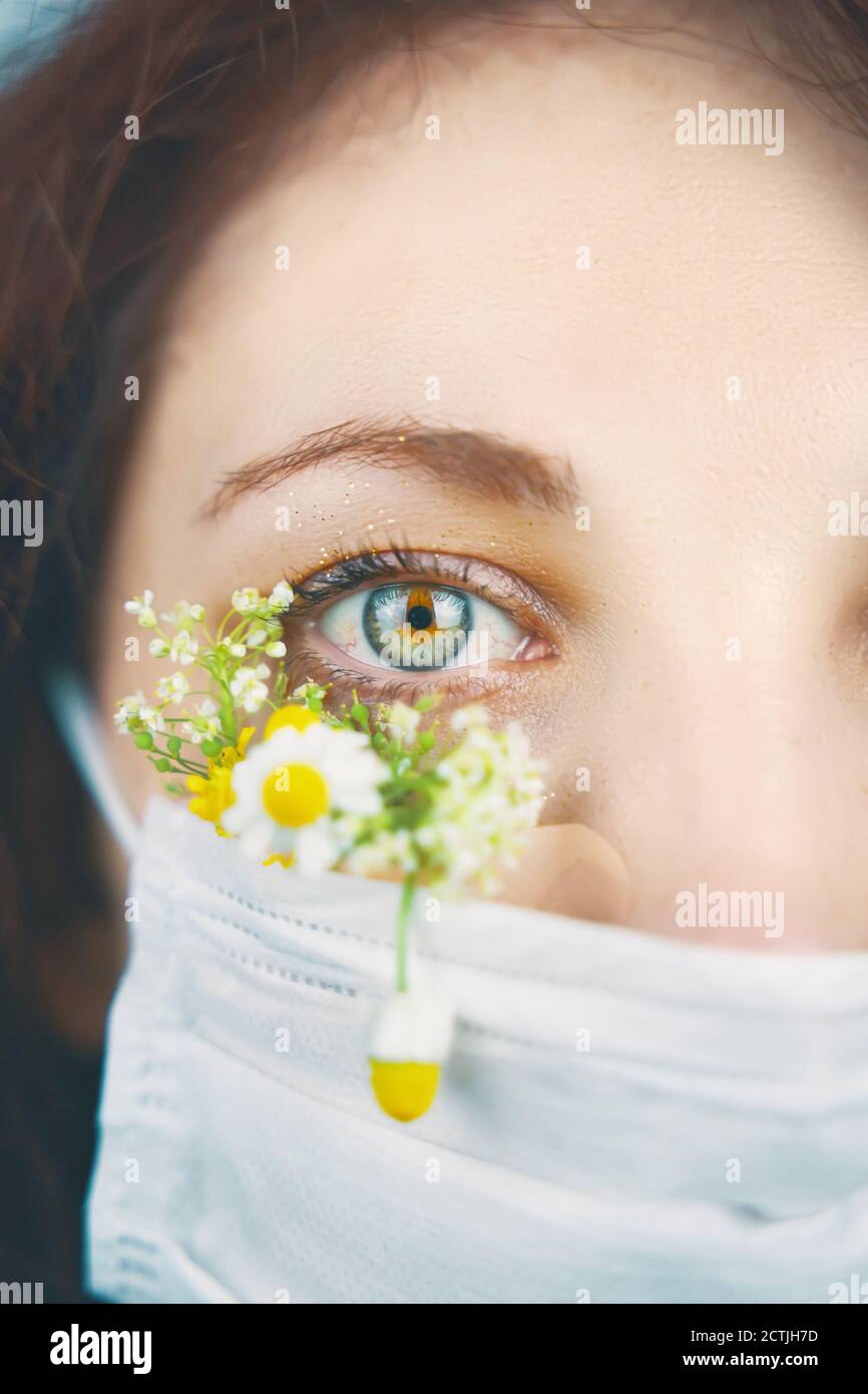 Ritratto dell'occhio macro. Giovane donna attraente in maschera floreale di fiori guardando la fotocamera in uno studio in una maschera durante la pandemia coronavirus, nuova tendenza primavera moda. Foto Stock