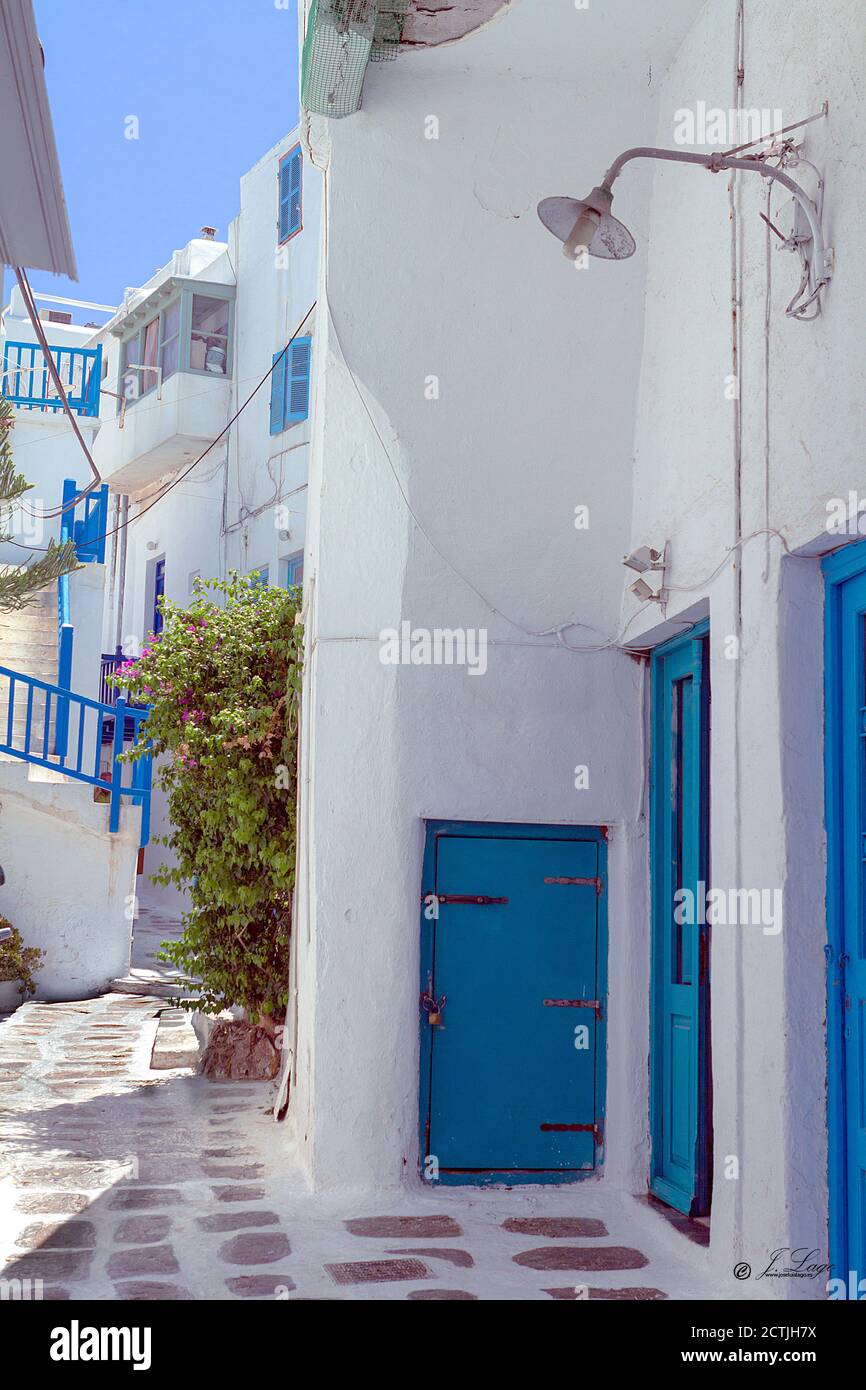 Strada stretta sull'isola greca di Mykonos, con le sue tipiche case bianche e le porte e le finestre blu Foto Stock