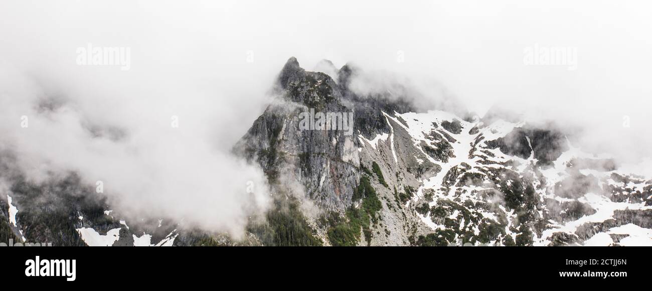 Spettacolare vetta di montagna circondata da nuvole in giornata bagnata Foto Stock